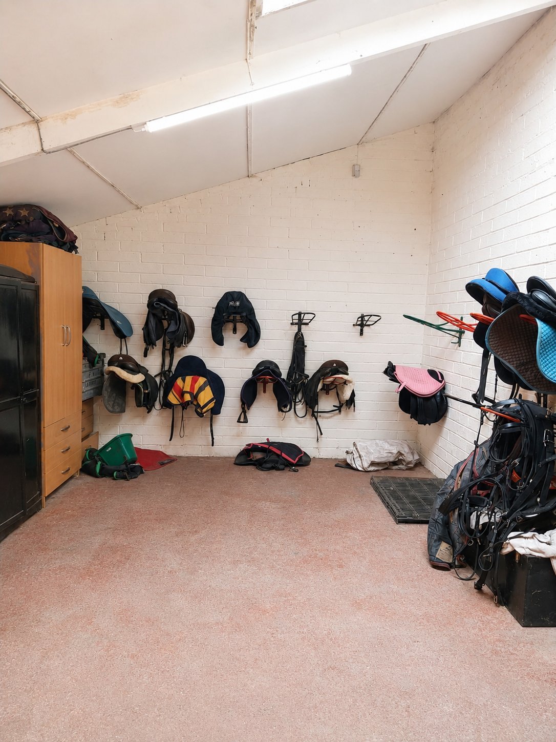 Bike storage room with helmets and cycling gear hanging on white tiled walls, bicycle on right side, wooden cabinet on left