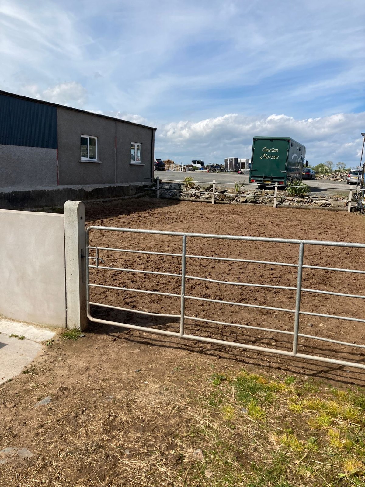 Metal farm gate in foreground with modular buildings and vintage truck in rural property yard