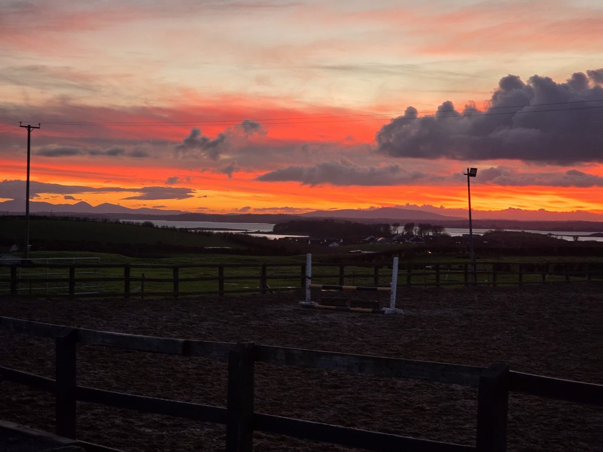 Vibrant orange and red sunset sky over a rural field with wooden fences and utility poles