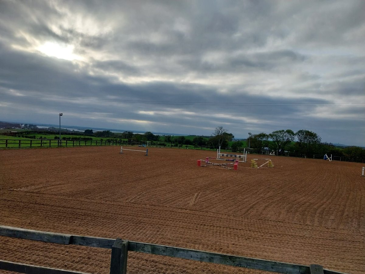 Empty equestrian arena with jump obstacles under overcast sky and rural landscape in background